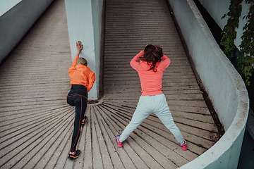 Image showing Two women warming up together and preparing for a morning run in an urban environment. Selective focus