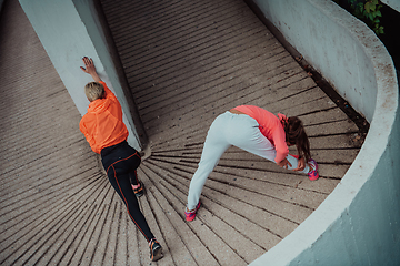 Image showing Two women warming up together and preparing for a morning run in an urban environment. Selective focus