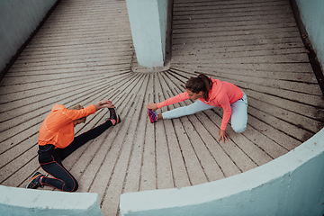 Image showing Two women warming up together and preparing for a morning run in an urban environment. Selective focus