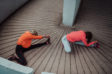 Image showing Two women warming up together and preparing for a morning run in an urban environment. Selective focus