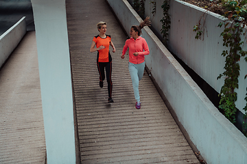 Image showing Two women in sports clothes running in a modern urban environment. The concept of a sporty and healthy lifestyle