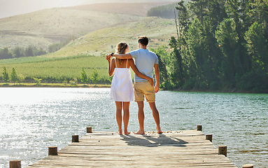 Image showing Couple on jetty by the lake, travel and relax together with nature and hug outdoor, love with care and bonding. Summer, holiday with man and woman back view, sunshine and relationship with trust