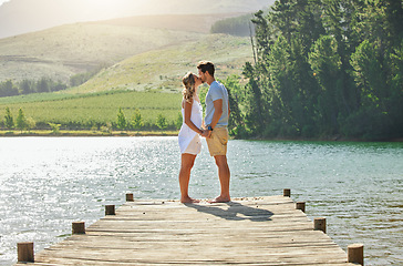 Image showing Couple, kissing and holding hands by the lake in romance for love, care and affection together in nature. Man and woman kiss by water on a romantic getaway, summer vacation or date by the lakeside