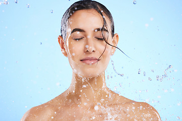 Image showing Water splash, beauty and skincare with a woman in studio on a blue background for hygiene or hydration. Relax, wellness and cleaning with an attractive young female in the shower for self care