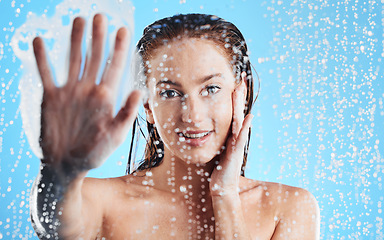 Image showing Shower portrait, water drops and woman hand against glass doing skin cleaning and beauty routine. Isolated, blue background and studio with a young female doing hair care and dermatology facial