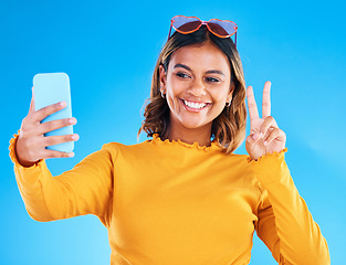 Image showing Selfie smile, studio and peace sign of a woman influencer taking a profile picture for social media. Isolated, blue background and emoji hands gesture of a gen z female with feeling happy and fun