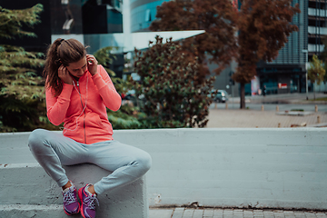 Image showing a woman in a sports outfit is resting in a city environment after a hard morning workout while using noiseless headphones