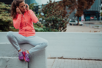 Image showing a woman in a sports outfit is resting in a city environment after a hard morning workout while using noiseless headphones