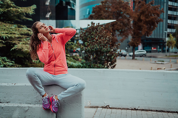 Image showing a woman in a sports outfit is resting in a city environment after a hard morning workout while using noiseless headphones