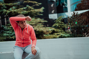 Image showing a woman in a sports outfit is resting in a city environment after a hard morning workout while using noiseless headphones