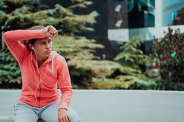 Image showing a woman in a sports outfit is resting in a city environment after a hard morning workout while using noiseless headphones