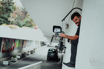 Image showing A professional cameraman with equipment and a stabilizer recoding two woman for a commercial advertisement as they run in an urban environment