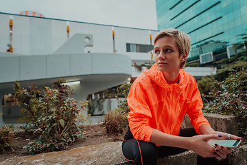 Image showing A woman in sports clothes sitting in a city environment and using smartphone after a hard morning workout