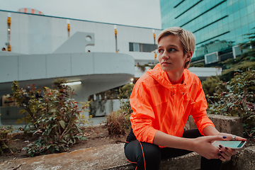 Image showing A woman in sports clothes sitting in a city environment and using smartphone after a hard morning workout