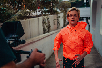 Image showing A professional cameraman with equipment and a stabilizer recoding woman for a commercial advertisement as they run in an urban environment