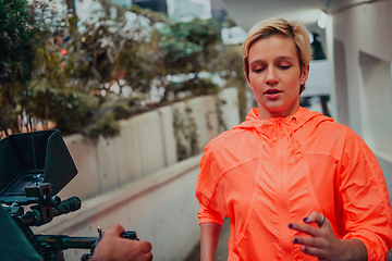 Image showing A professional cameraman with equipment and a stabilizer recoding woman for a commercial advertisement as they run in an urban environment