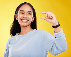 Image showing Hand gesture, pinch and measure with a woman on a yellow background in studio to show a size. Smile, review and icon or symbol with an attractive young female posing on a color wall for growth