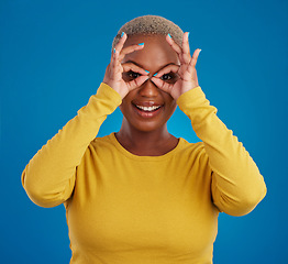 Image showing Black woman, binocular hands and eyes in studio portrait for comic funny face with smile, fashion and happy. Student girl, model and ok hand gesture with happiness, youth and pride by blue background