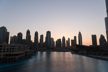 Image showing Dubai singing fountains at night lake view between skyscrapers. City skyline in dusk modern architecture in UAE capital downtown.