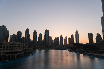 Image showing Dubai singing fountains at night lake view between skyscrapers. City skyline in dusk modern architecture in UAE capital downtown.