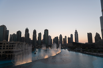 Image showing Dubai singing fountains at night lake view between skyscrapers. City skyline in dusk modern architecture in UAE capital downtown.