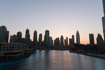 Image showing Dubai singing fountains at night lake view between skyscrapers. City skyline in dusk modern architecture in UAE capital downtown.