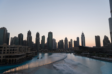 Image showing Dubai singing fountains at night lake view between skyscrapers. City skyline in dusk modern architecture in UAE capital downtown.