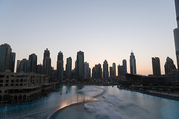 Image showing Dubai singing fountains at night lake view between skyscrapers. City skyline in dusk modern architecture in UAE capital downtown.