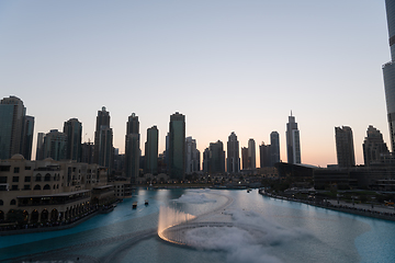 Image showing Dubai singing fountains at night lake view between skyscrapers. City skyline in dusk modern architecture in UAE capital downtown.