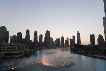 Image showing Dubai singing fountains at night lake view between skyscrapers. City skyline in dusk modern architecture in UAE capital downtown.