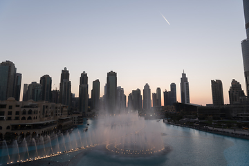 Image showing Dubai singing fountains at night lake view between skyscrapers. City skyline in dusk modern architecture in UAE capital downtown.