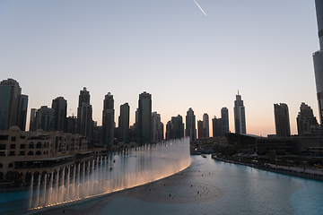 Image showing Dubai singing fountains at night lake view between skyscrapers. City skyline in dusk modern architecture in UAE capital downtown.