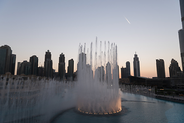 Image showing Dubai singing fountains at night lake view between skyscrapers. City skyline in dusk modern architecture in UAE capital downtown.