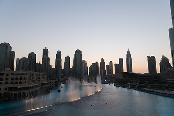 Image showing Dubai singing fountains at night lake view between skyscrapers. City skyline in dusk modern architecture in UAE capital downtown.