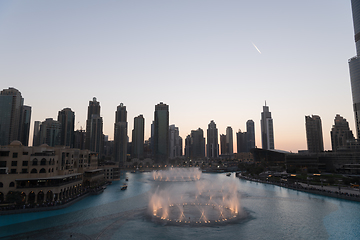 Image showing Dubai singing fountains at night lake view between skyscrapers. City skyline in dusk modern architecture in UAE capital downtown.