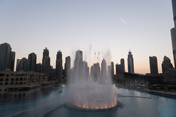 Image showing Dubai singing fountains at night lake view between skyscrapers. City skyline in dusk modern architecture in UAE capital downtown.