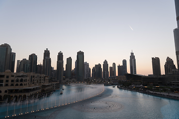 Image showing Dubai singing fountains at night lake view between skyscrapers. City skyline in dusk modern architecture in UAE capital downtown.