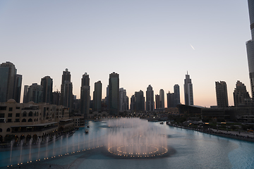 Image showing Dubai singing fountains at night lake view between skyscrapers. City skyline in dusk modern architecture in UAE capital downtown.