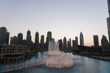 Image showing Dubai singing fountains at night lake view between skyscrapers. City skyline in dusk modern architecture in UAE capital downtown.