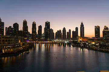 Image showing Dubai singing fountains at night lake view between skyscrapers. City skyline in dusk modern architecture in UAE capital downtown.