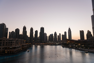 Image showing Dubai singing fountains at night lake view between skyscrapers. City skyline in dusk modern architecture in UAE capital downtown.