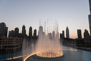 Image showing Dubai singing fountains at night lake view between skyscrapers. City skyline in dusk modern architecture in UAE capital downtown.