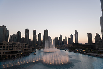 Image showing Dubai singing fountains at night lake view between skyscrapers. City skyline in dusk modern architecture in UAE capital downtown.