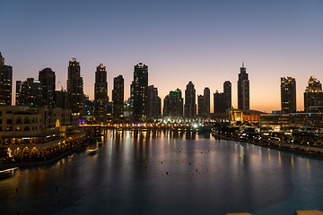 Image showing Dubai singing fountains at night lake view between skyscrapers. City skyline in dusk modern architecture in UAE capital downtown.