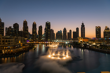 Image showing Dubai singing fountains at night lake view between skyscrapers. City skyline in dusk modern architecture in UAE capital downtown.