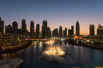 Image showing Dubai singing fountains at night lake view between skyscrapers. City skyline in dusk modern architecture in UAE capital downtown.