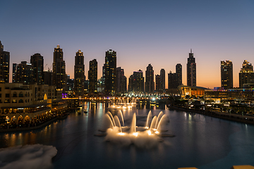 Image showing Dubai singing fountains at night lake view between skyscrapers. City skyline in dusk modern architecture in UAE capital downtown.