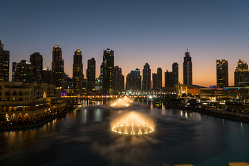 Image showing Dubai singing fountains at night lake view between skyscrapers. City skyline in dusk modern architecture in UAE capital downtown.