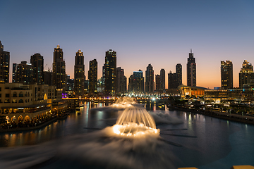 Image showing Dubai singing fountains at night lake view between skyscrapers. City skyline in dusk modern architecture in UAE capital downtown.