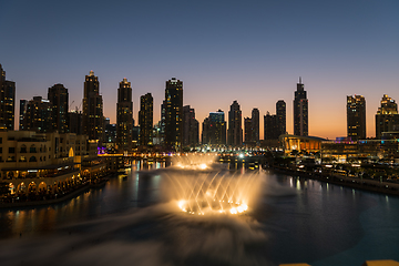 Image showing Dubai singing fountains at night lake view between skyscrapers. City skyline in dusk modern architecture in UAE capital downtown.